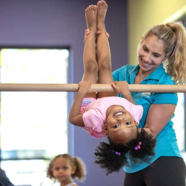 A girl upside down on a balance bar doing gymnastics with a coach