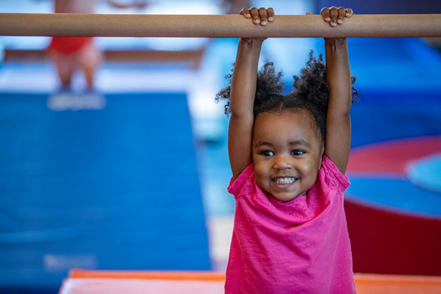 young girl hanging from a bar by her hands